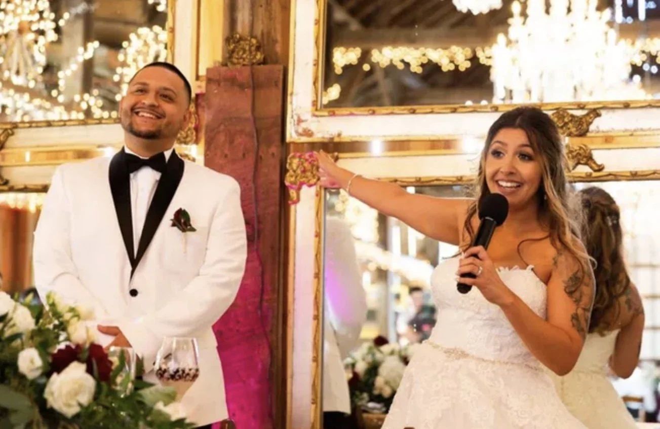 Groom and bride speaking into a wireless microphone at their barn wedding reception